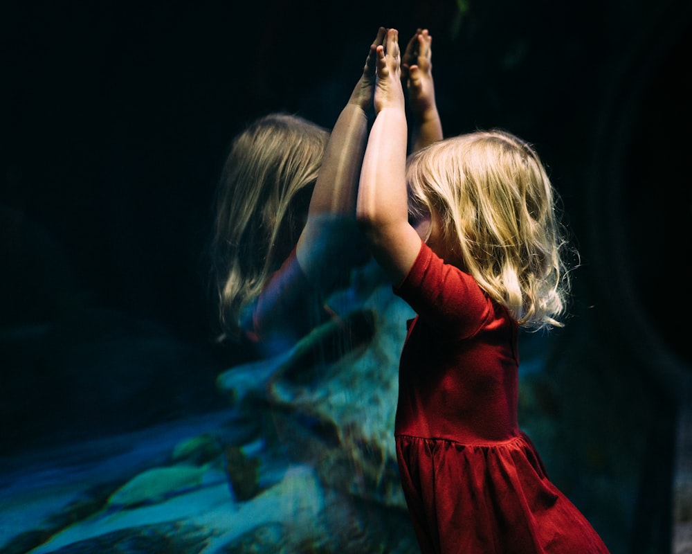Mädchen, das sich auf ein Glasaquarium stützt und ihre beiden Hände hebt