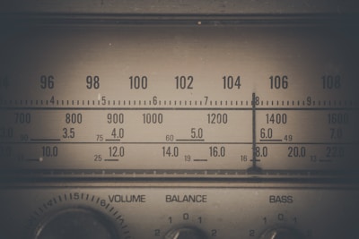 A vintage radio tuner with an analog dial displaying various frequency numbers. The design features dials labeled as volume, balance, and bass.