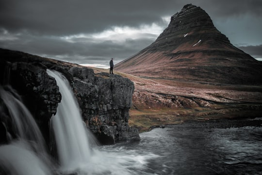 photography of man standing of top of mountain in Kirkjufell Iceland