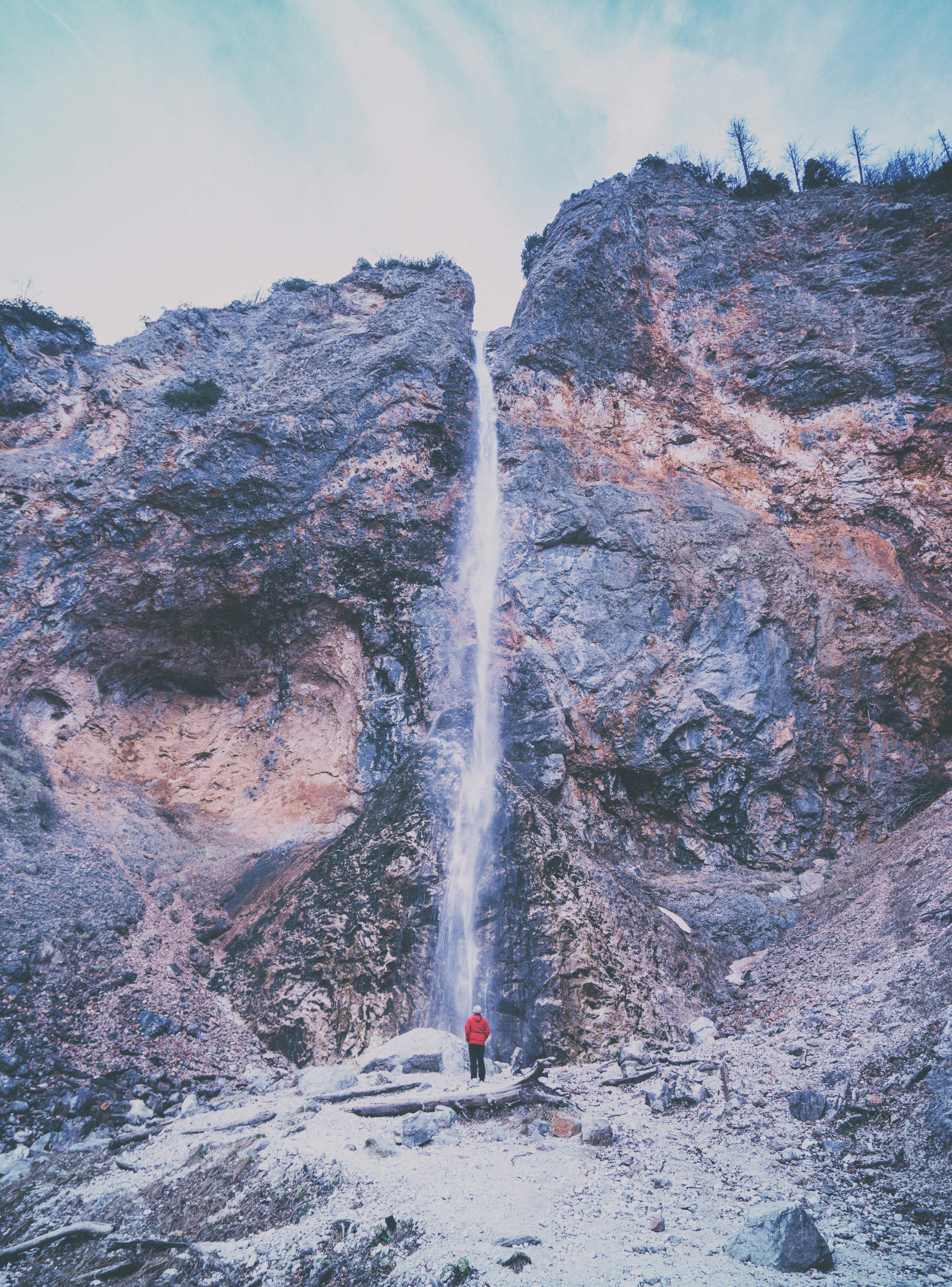 person wearing red jacket standing near waterfalls