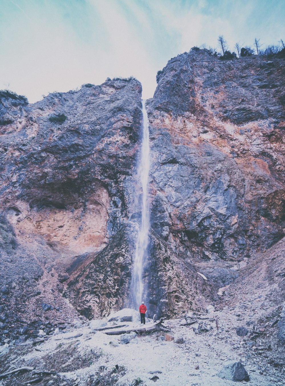 Person in roter Jacke, die in der Nähe von Wasserfällen steht