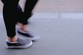 A person walking in baggy trousers and a loose shirt, captured mid-step on a city sidewalk.
