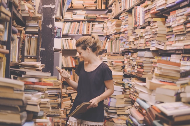 A smiling woman dusting shelves filled with books and plants