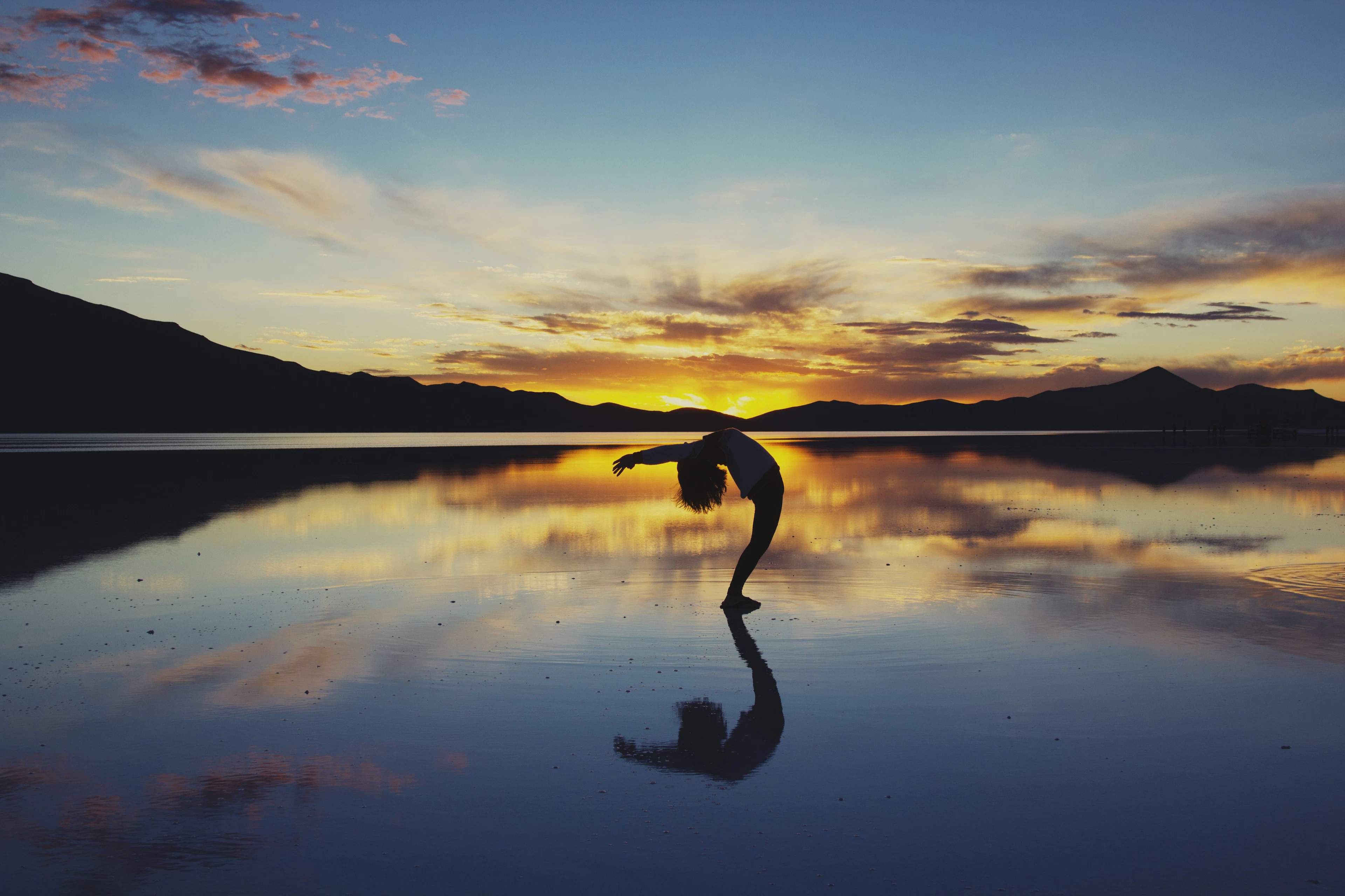 Silhouette of a person practising yoga against a wide open sky at first light