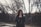smiling woman holding smartphone standing near fence with trees during daytime