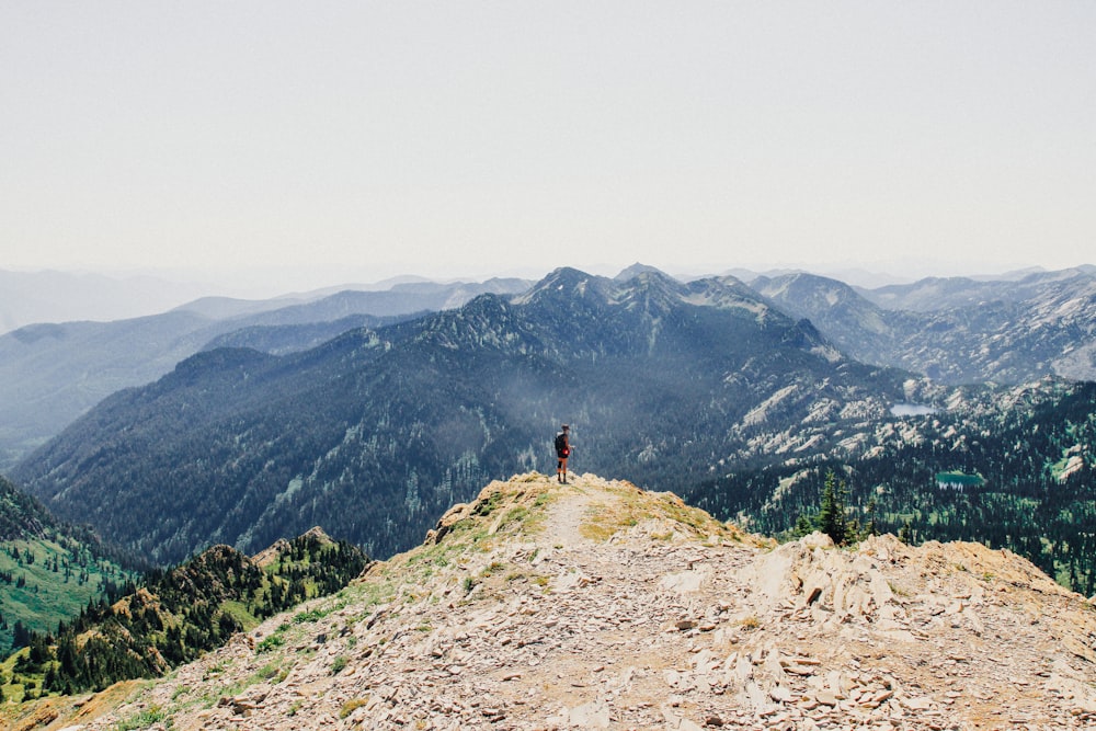 person standing on mountain cliff under white sky