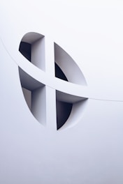 The image features an architectural design with smooth white surfaces and geometric cutouts, creating a modern and abstract aesthetic. The cutouts form curved and intersecting shapes, adding depth and visual interest.