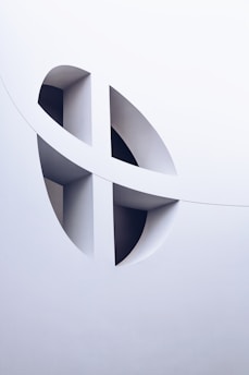 The image features an architectural design with smooth white surfaces and geometric cutouts, creating a modern and abstract aesthetic. The cutouts form curved and intersecting shapes, adding depth and visual interest.