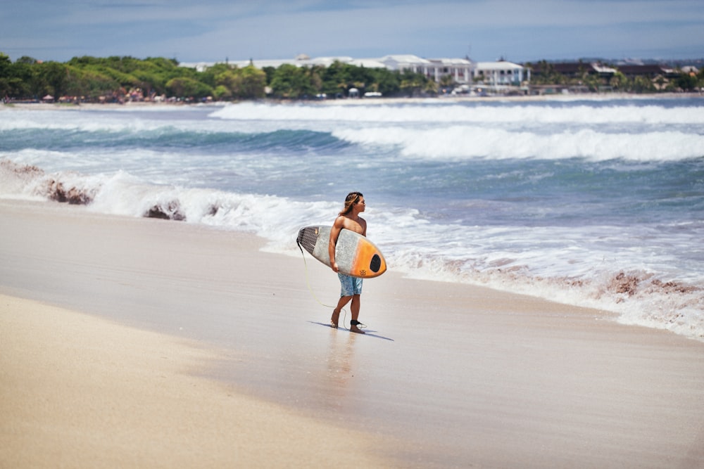 해변 근처에 서 있는 노란색과 흰색 서핑 보드를 들고 있는 남자