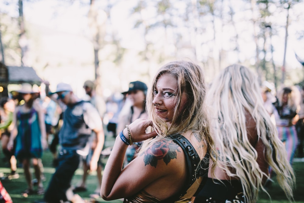 A blond woman with a rose tattoo on her arm looking back at the camera at an outdoor party