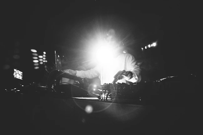 Dynamic black-and-white photo capturing a DJ mid-set, bathed in contrasting light and shadow.