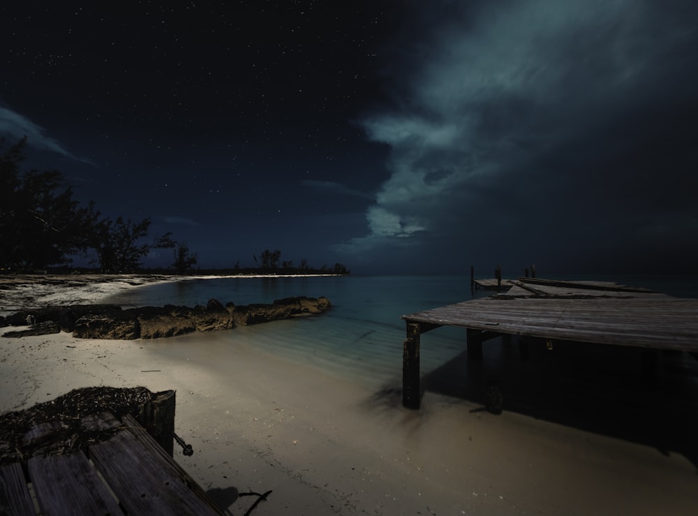 Muelle de madera marrón y cuerpo de agua bajo cielo negro durante la noche