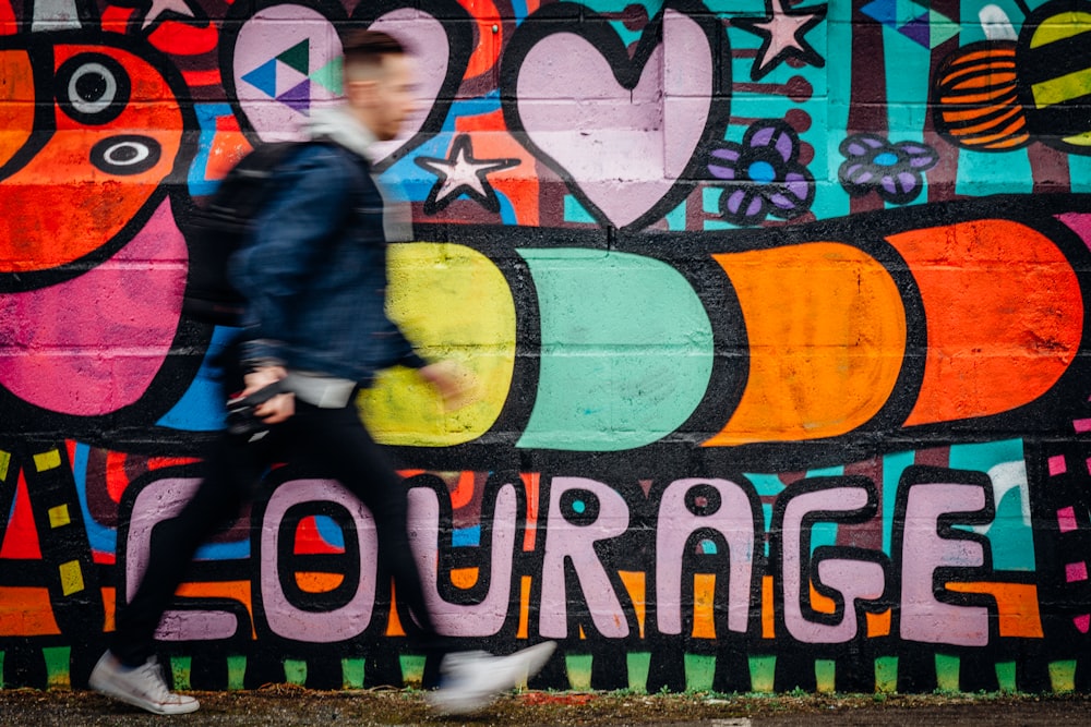 homem caminhando ao lado de muro de grafite