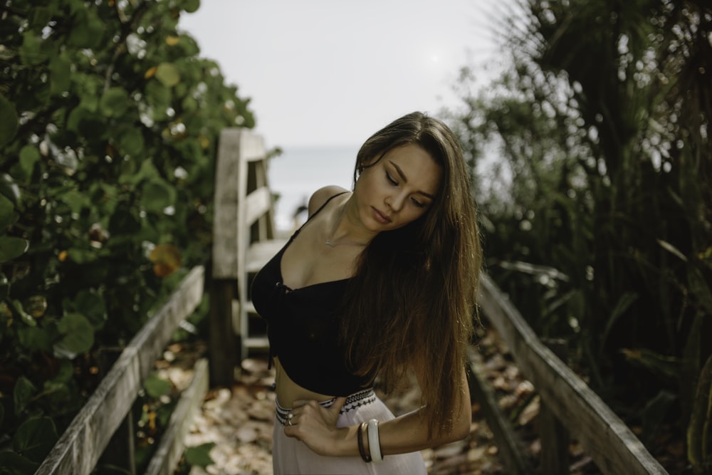 woman standing on bridge in between trees during daytime