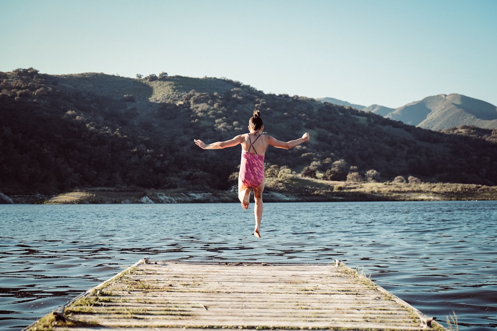 woman wearing pink top jumping towards water during daytime