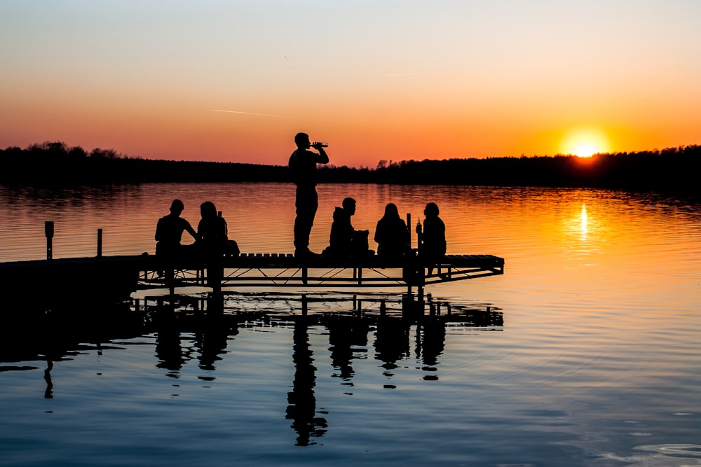 group of people on wooden dock during sunset in silhouette photography