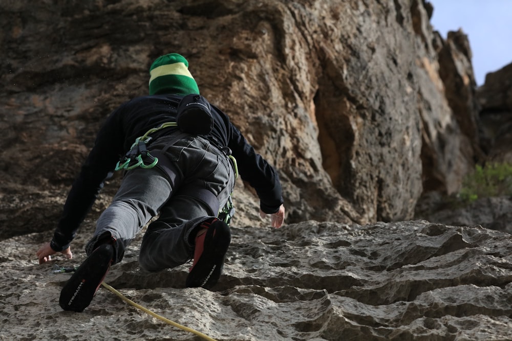 Hombre con chaqueta negra y pantalones verdes escalando en la montaña rocosa marrón durante el día
