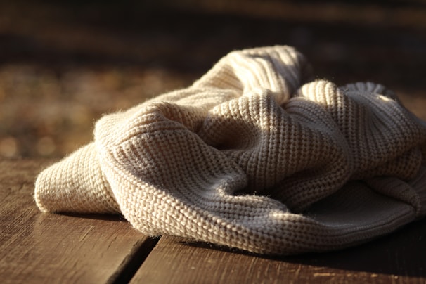 A close-up of a soft, cream-colored knit sweater draped over a wooden chair in natural light