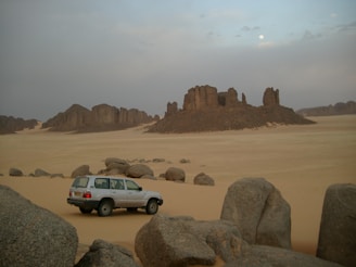 A serene desert landscape with a lone 4x4 parked near red sandstone formations at sunset.