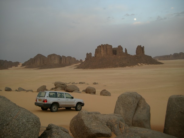 A serene desert landscape with a lone 4x4 parked near red sandstone formations at sunset.