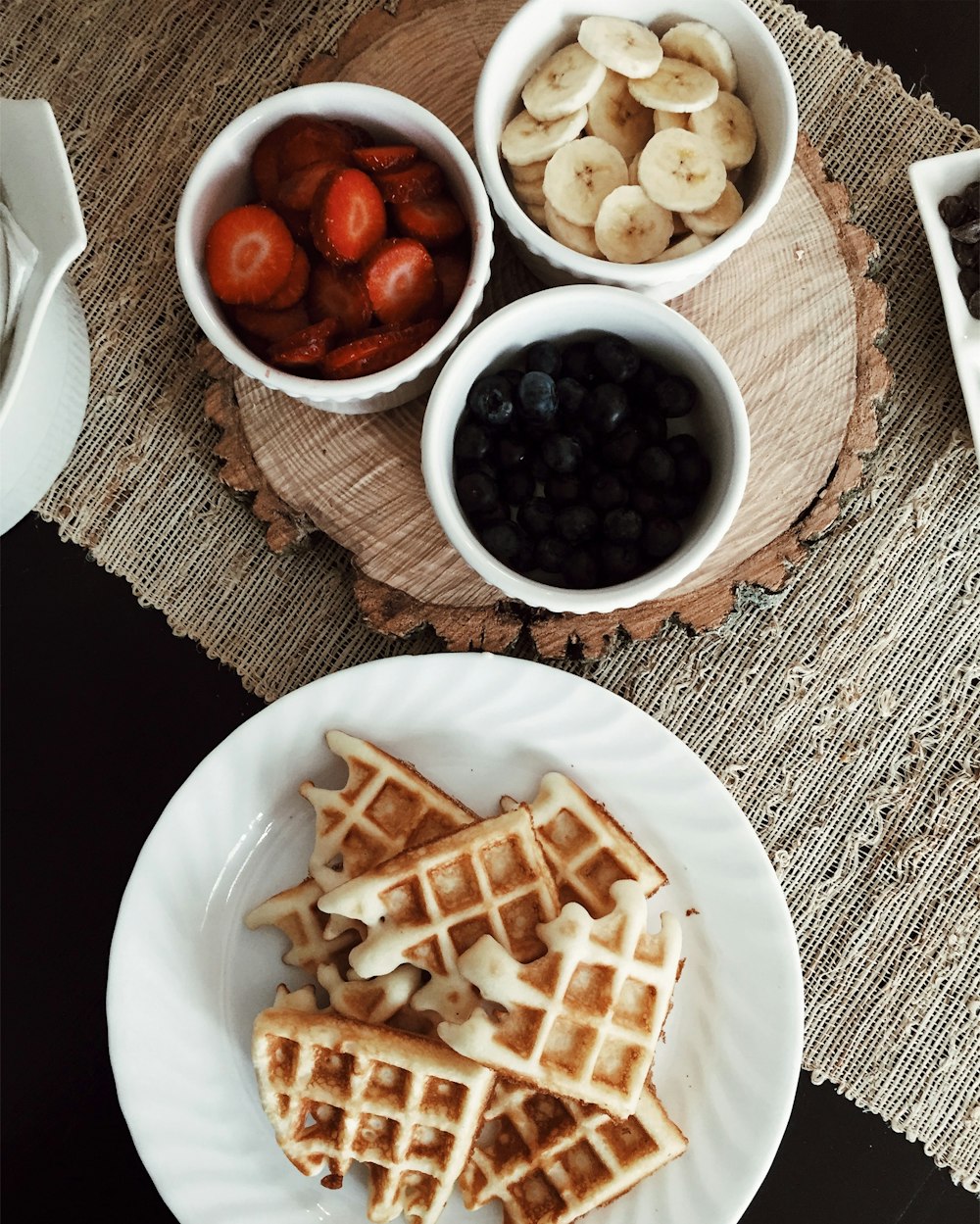 foto de waffles ao lado de tigelas de morangos, banana e bagas pretas