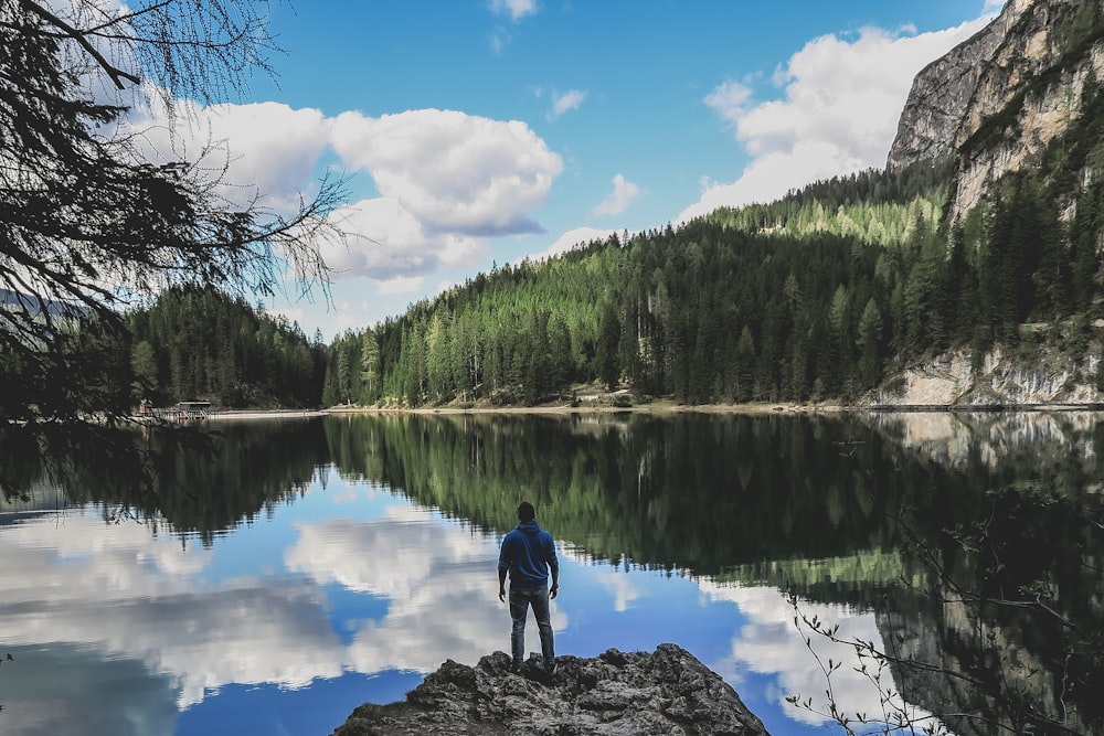 Homem na jaqueta azul em pé na rocha perto do lago durante o dia