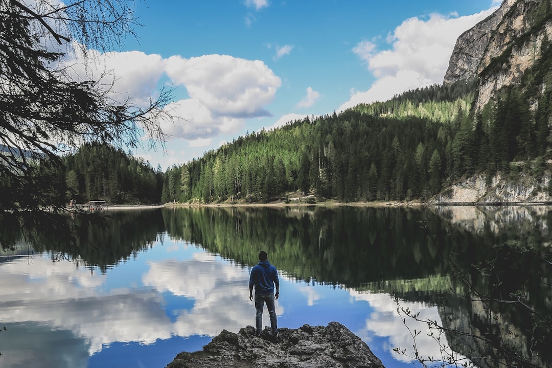 man in blue jacket standing on rock near lake during daytime