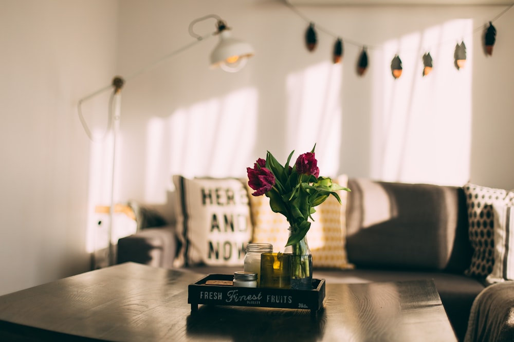 selective focus photography of two red petaled flowers in vase on coffee table in living room