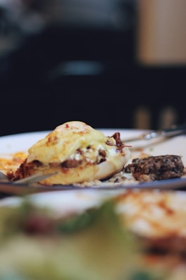 A close-up of a gourmet dish featuring a stuffed pastry topped with melted cheese, alongside a small portion of what appears to be a vegetable or grain salad. The background is softly blurred, emphasizing the dish.