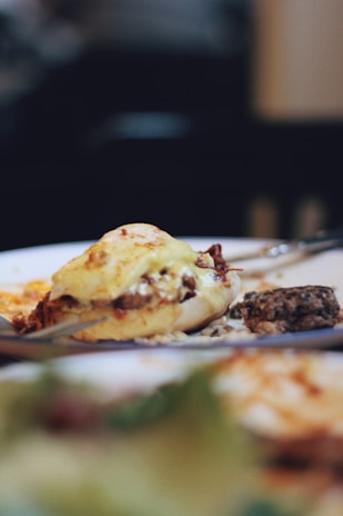 A close-up of a gourmet dish featuring a stuffed pastry topped with melted cheese, alongside a small portion of what appears to be a vegetable or grain salad. The background is softly blurred, emphasizing the dish.