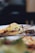 A close-up of a gourmet dish featuring a stuffed pastry topped with melted cheese, alongside a small portion of what appears to be a vegetable or grain salad. The background is softly blurred, emphasizing the dish.