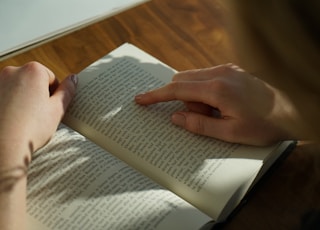 person reading book on brown wooden table taken at daytome