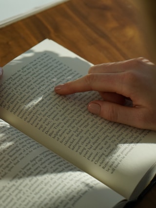 person reading book on brown wooden table taken at daytome