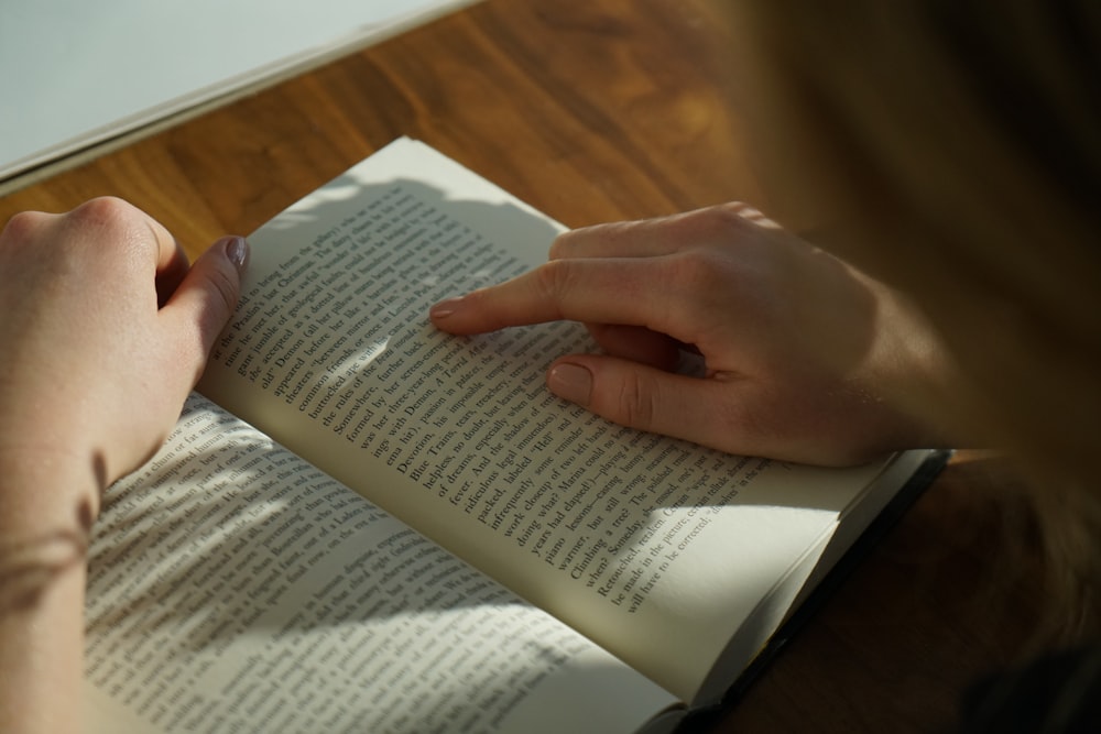 Person, die ein Buch auf braunem Holztisch liest, aufgenommen bei Daytome