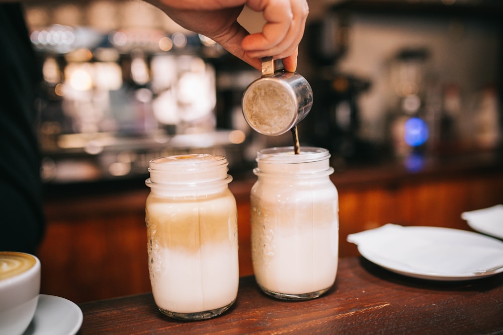 hand holding stainless steel cup pouring coffee on glass jars