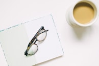 A pair of teyes sunglasses placed beside a leather-bound notebook and coffee cup, evoking a stylish daily routine.