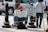 A person is sitting on the sidewalk holding a sign that reads 'I'm just hungry'. They are wearing a red cap and jeans. Around them are street posts and a sign instructing pedestrians to cross using the other side. The background includes a parked vehicle and another person standing nearby.