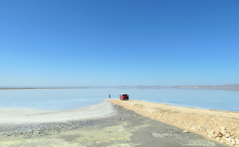 man standing near body of water and red car during daytime