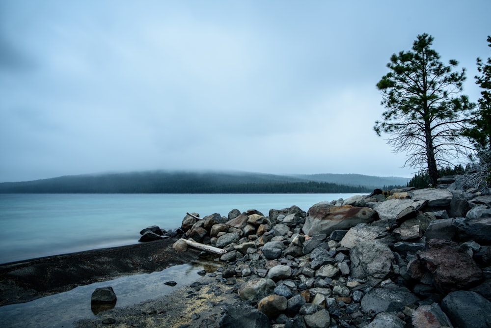 rocks beside body of water under white and gray sky