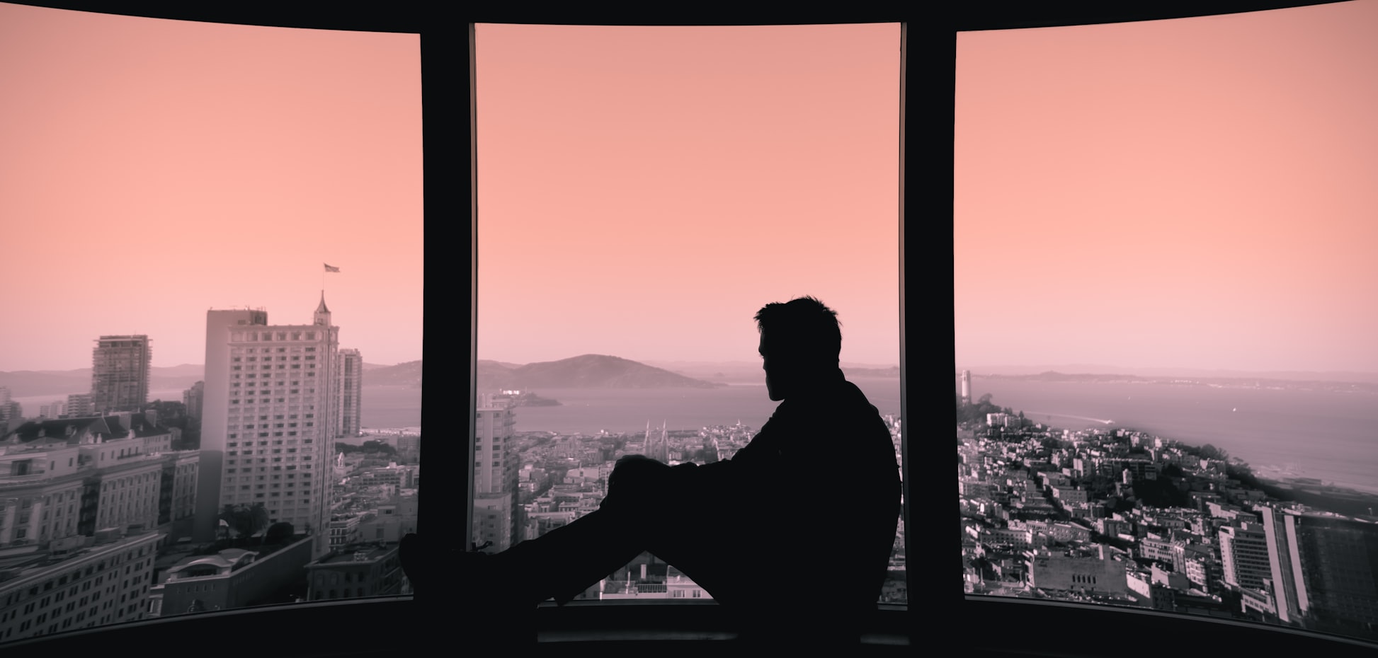 A silhouette of a man sitting on a windowsill and looking out the window