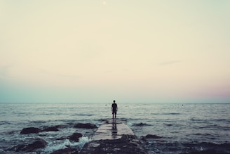 silhouette of person standing on sea dock under cloudy sky