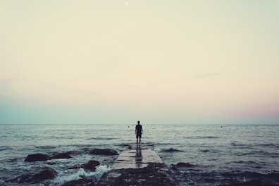 silhouette of person standing on sea dock under cloudy sky