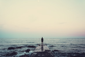 silhouette of person standing on sea dock under cloudy sky