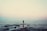 silhouette of person standing on sea dock under cloudy sky