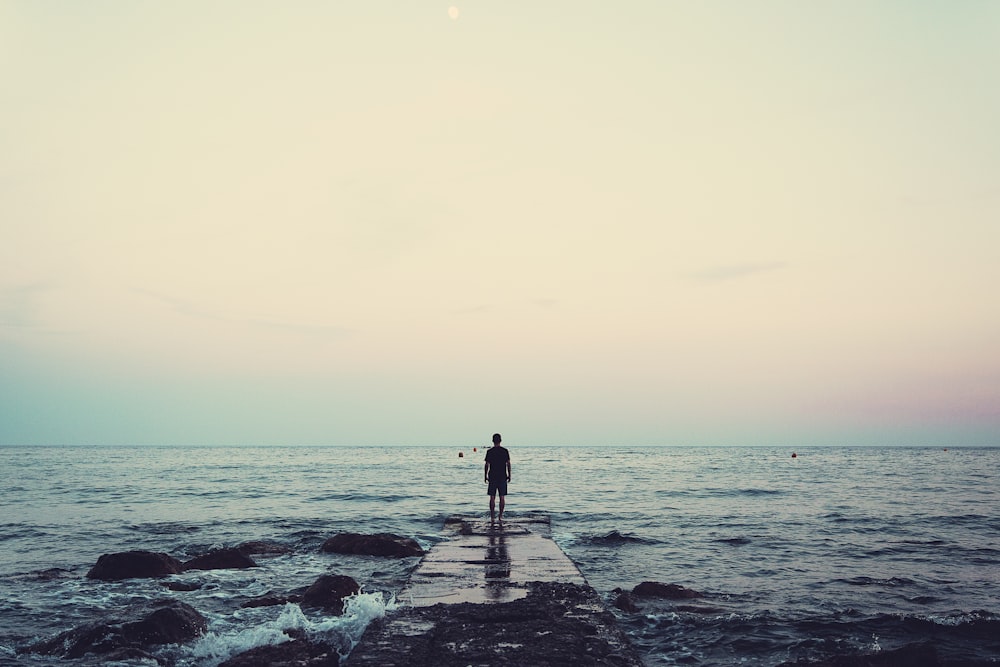 silhouette of person standing on sea dock under cloudy sky