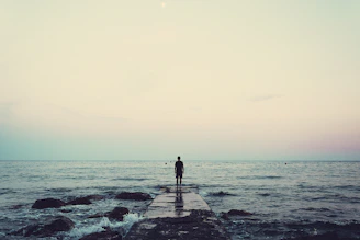 silhouette of person standing on sea dock under cloudy sky