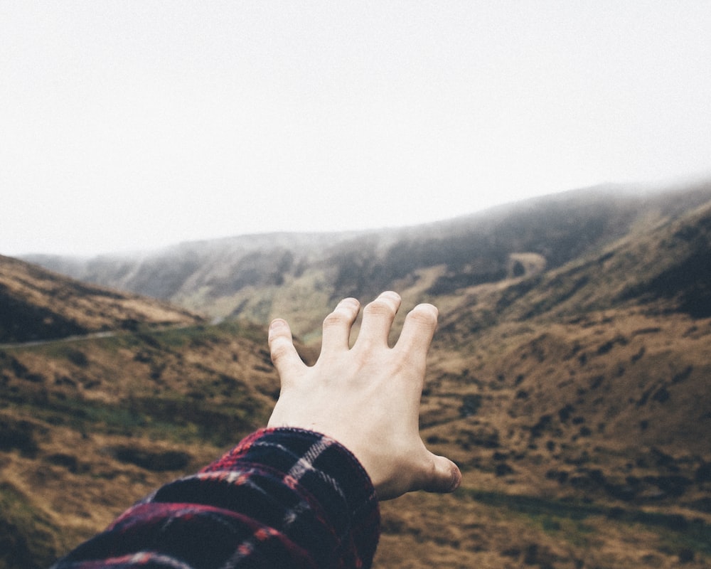 Photographie de point de vue d’une personne levant la main vers les montagnes