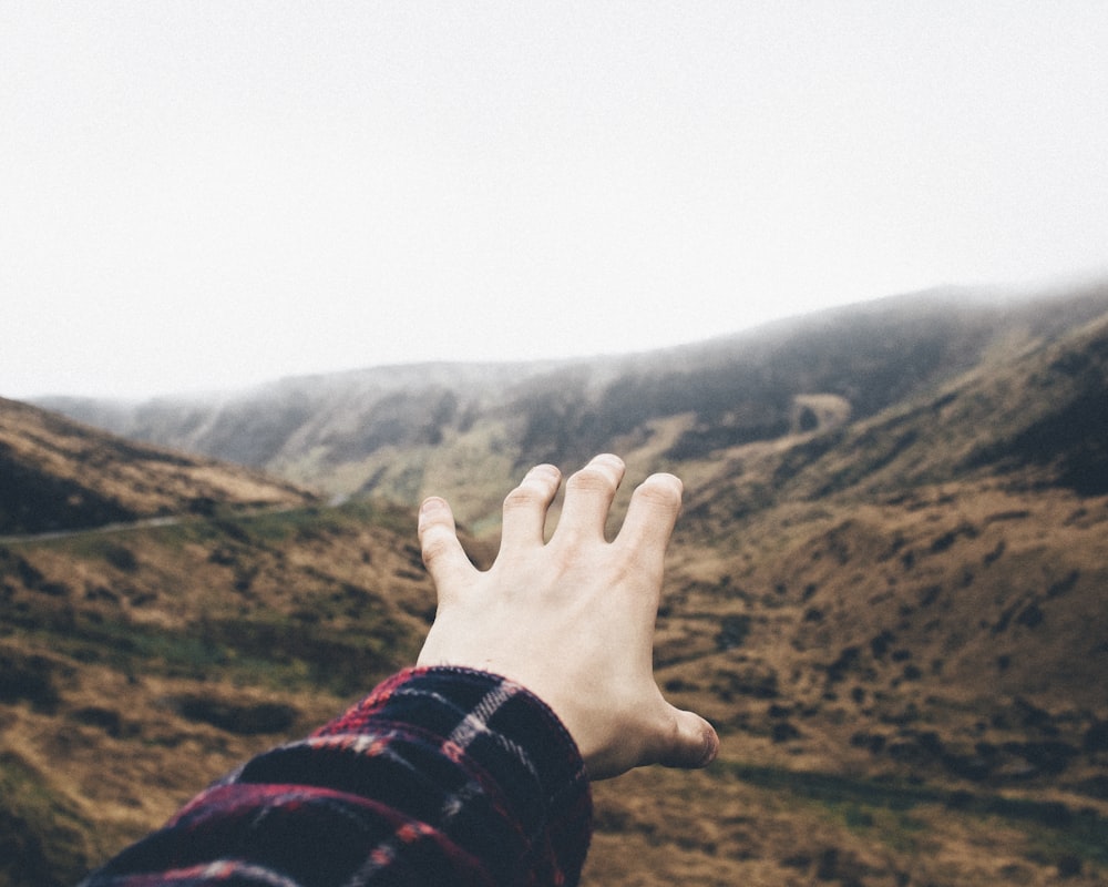 Fotografía de punto de vista de persona levantando la mano hacia las montañas