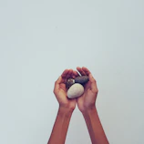 Close-up of hands holding smooth river stones with soft beige background.