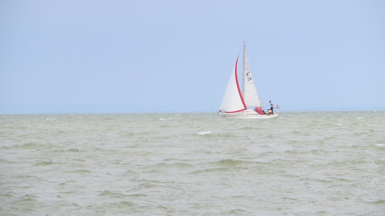 A friendly instructor guiding a student on a small sailboat under clear blue skies.